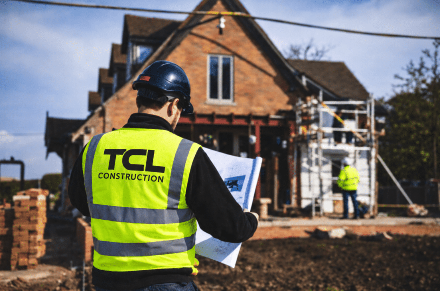 TCL Construction builder in branded hi-vis reviewing plans on site at a new home build in Essex